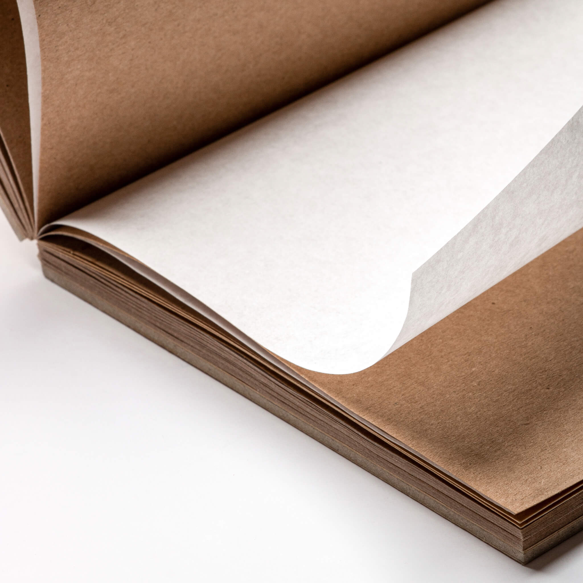 Close-up of a lay-flat square sketchbook showing kraft paper pages with an interleaved tracing sheet between sections