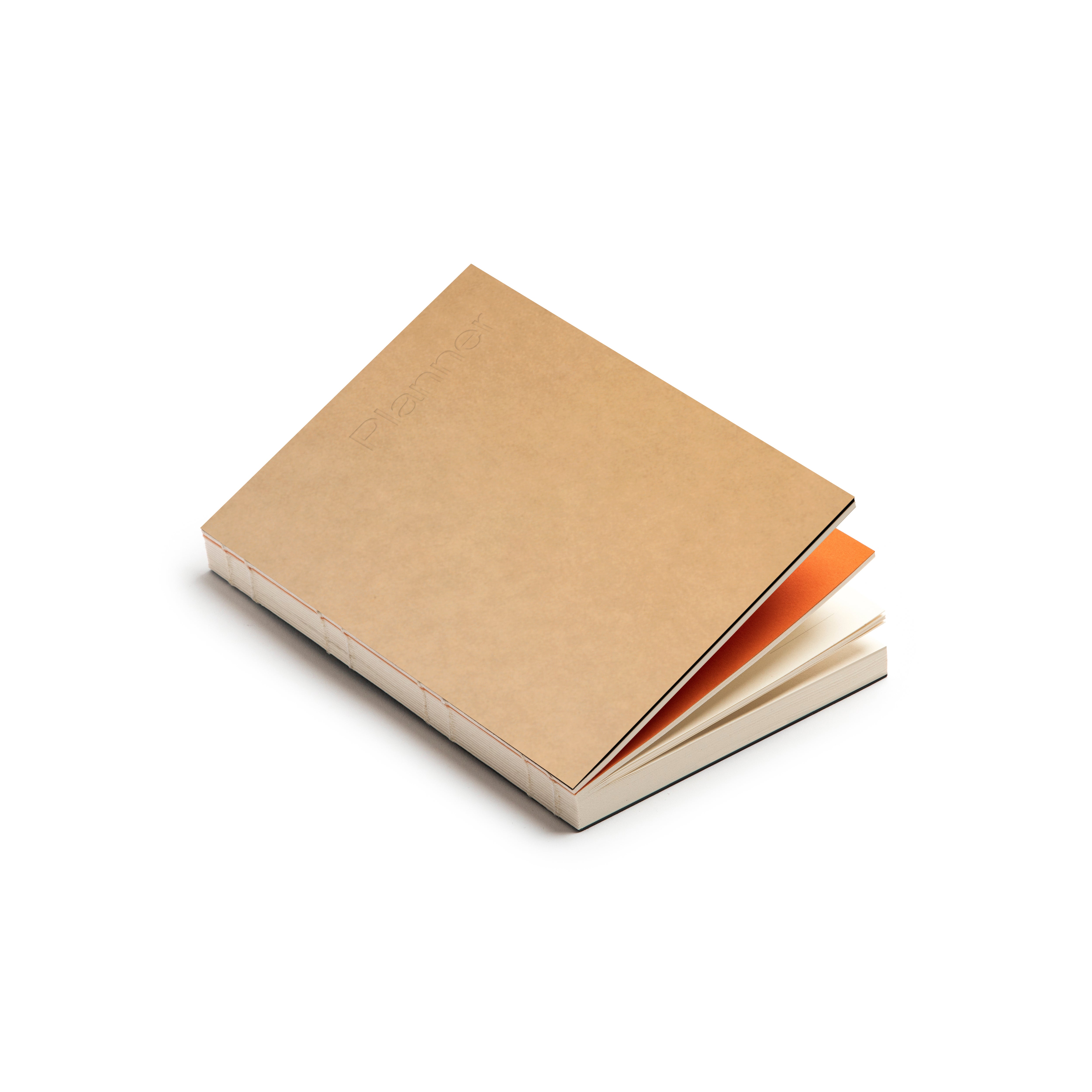 Basenotes Planner with kraft cover and orange divider, featuring exposed spine stitching and FSC-certified cream pages in a lay-flat design.