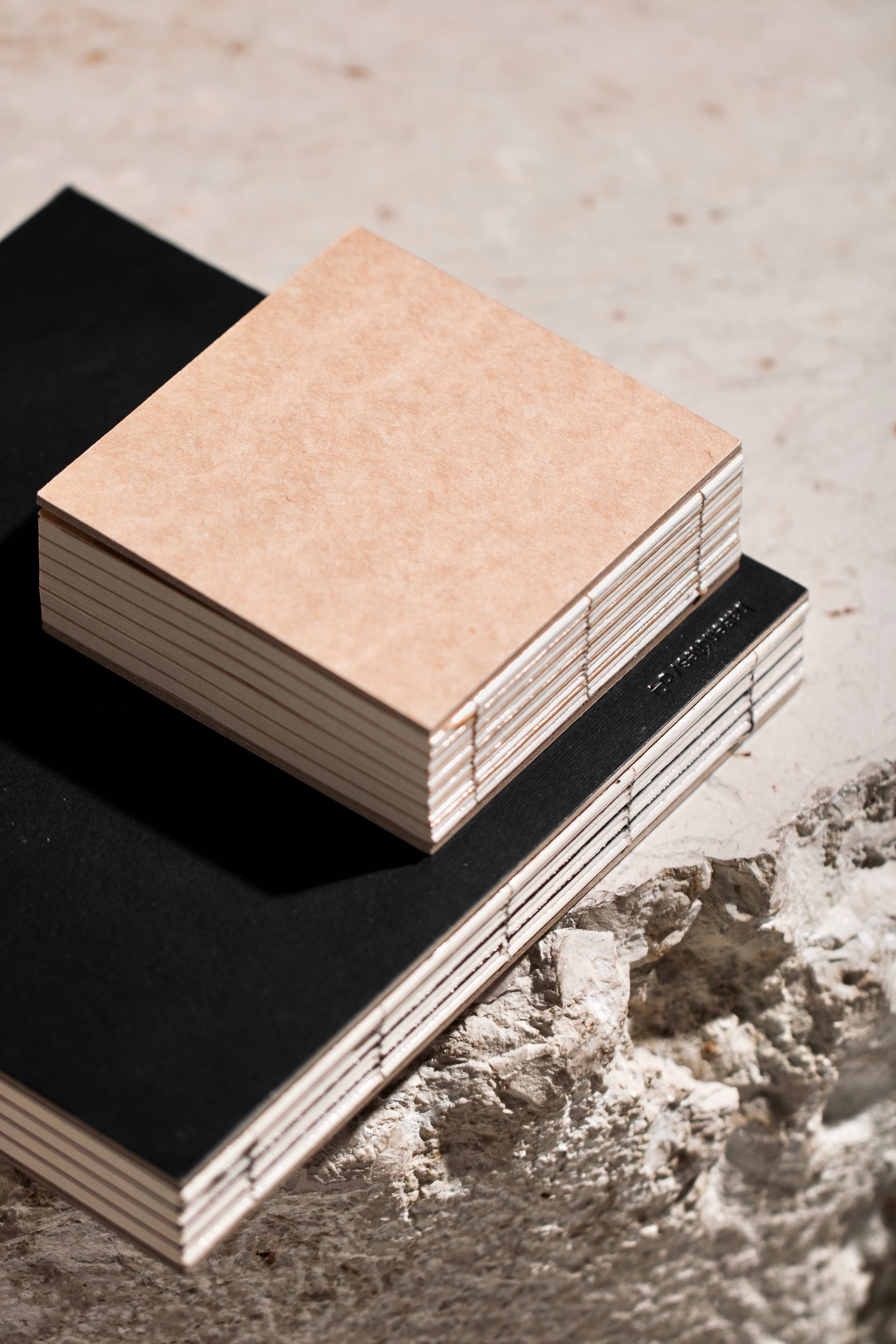 Stack of handmade basenotes notebooks with kraft and black covers on a textured surface