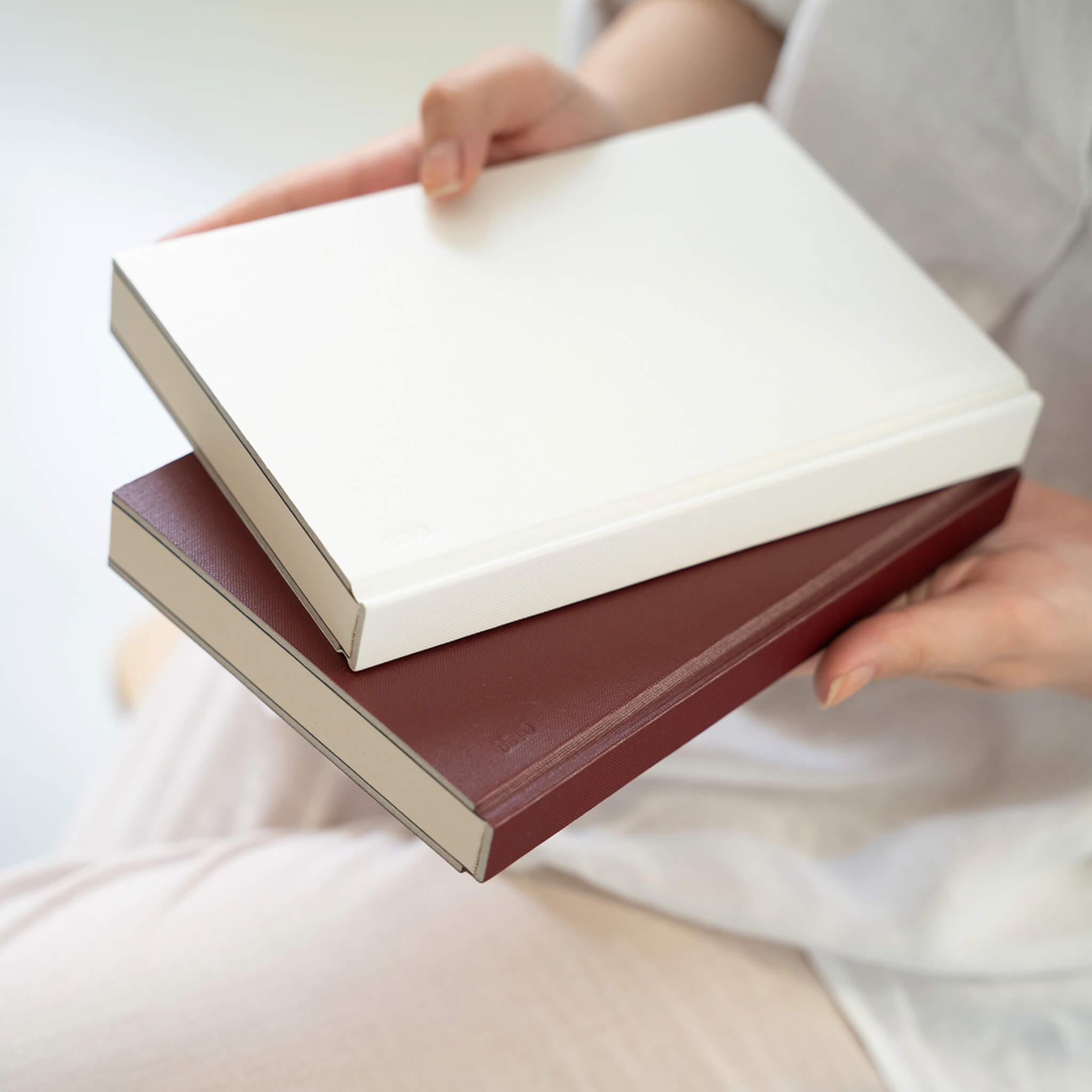 Person holding basenotes 0128 Notebooks in maroon and white covers, showing their refined hardcover texture.