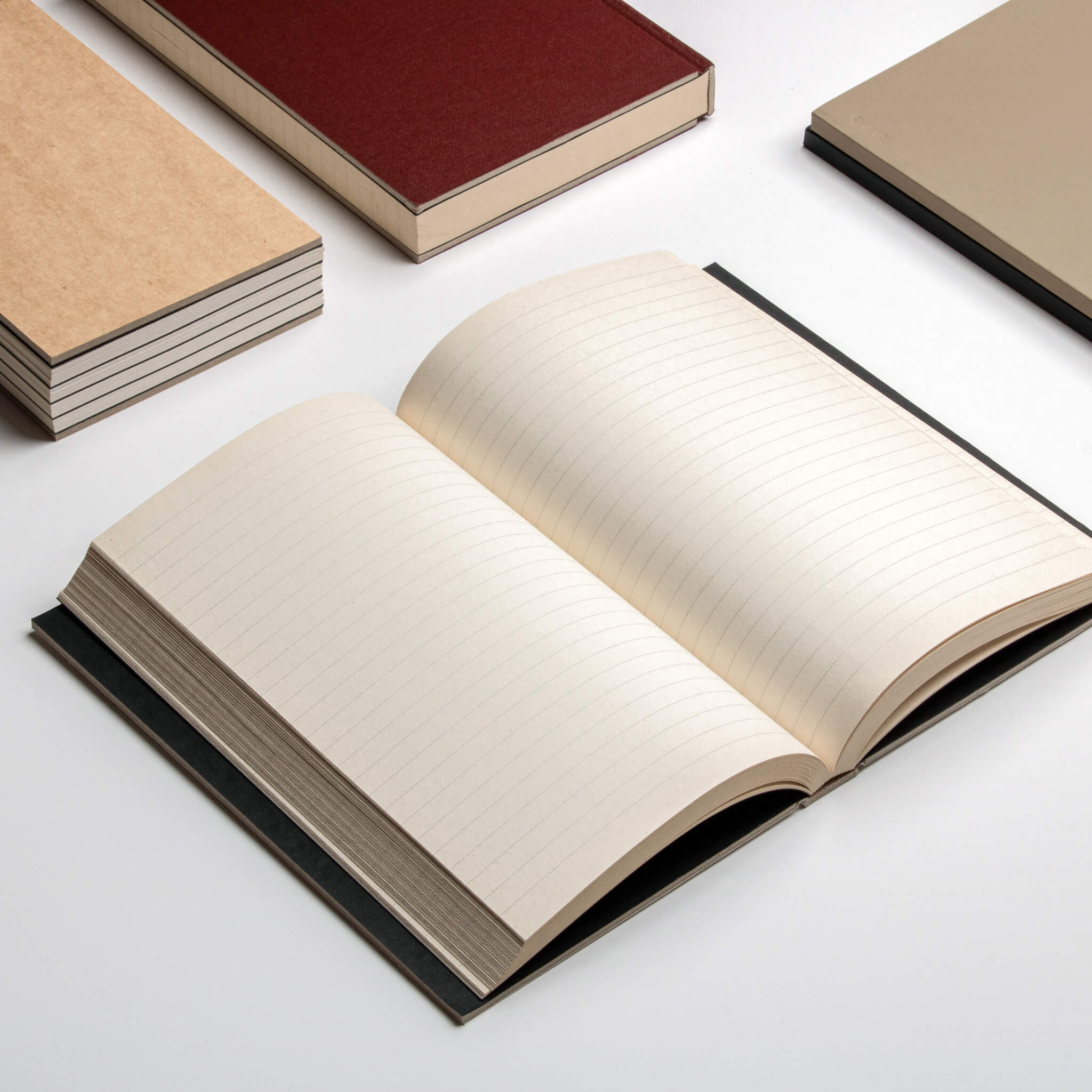 Open basenotes 0128 Notebook surrounded by other notebooks on a minimal white surface, displaying lined acid-free pages.