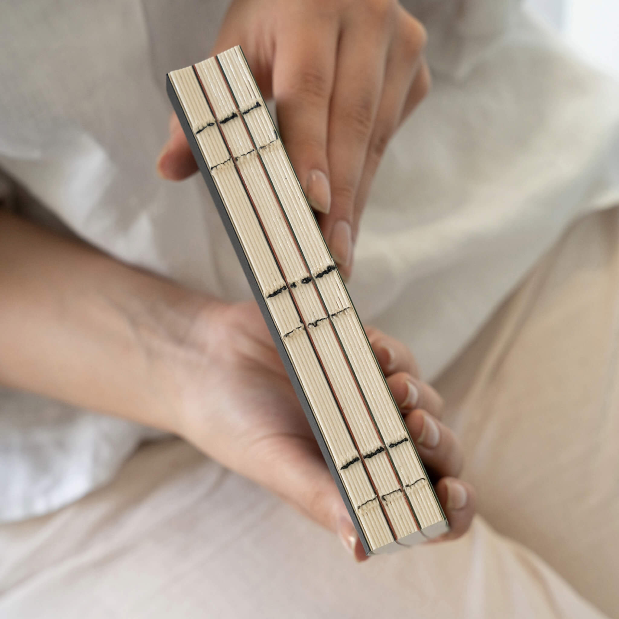 Hand-held view of basenotes 0144 Notebook spine showing exposed black stitching across three sewn sections.