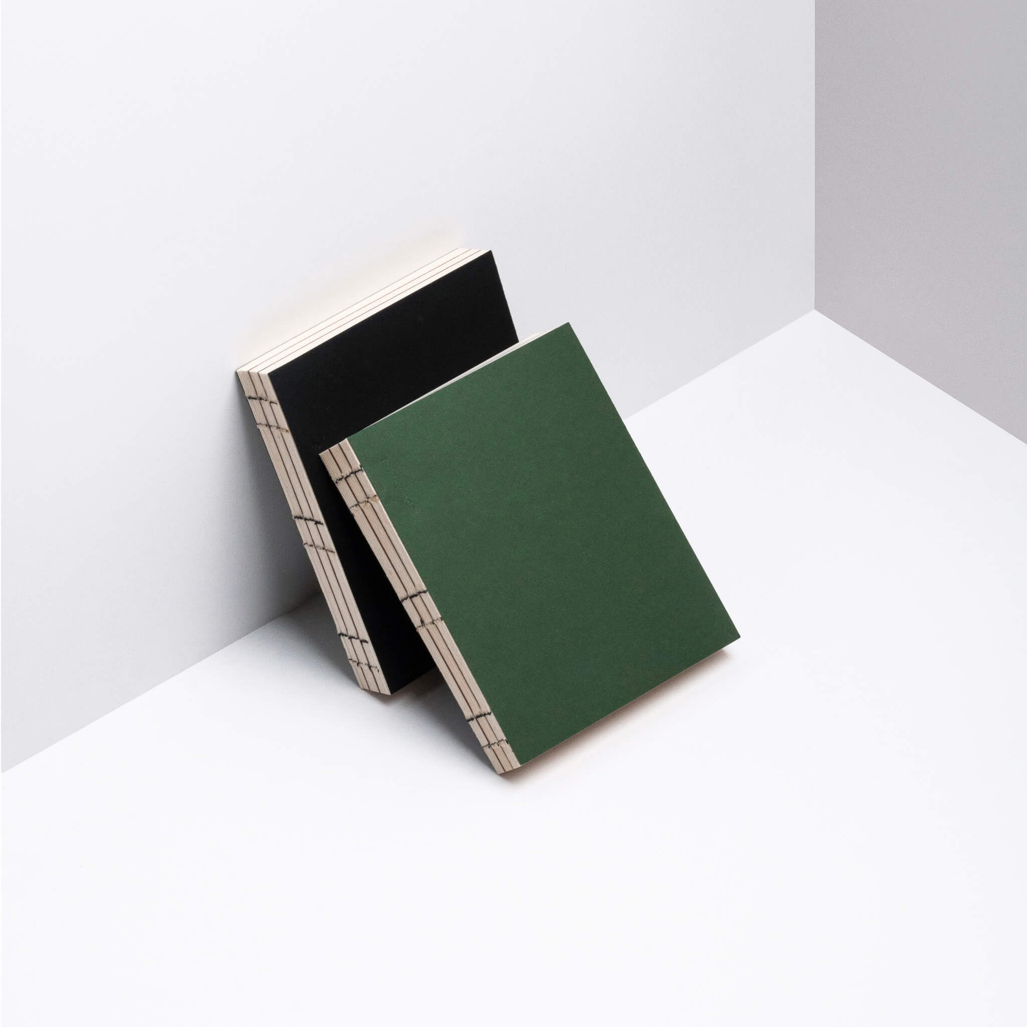 basenotes 0144 notebooks in green and black covers leaning together, featuring exposed spine stitching and minimal aesthetic.