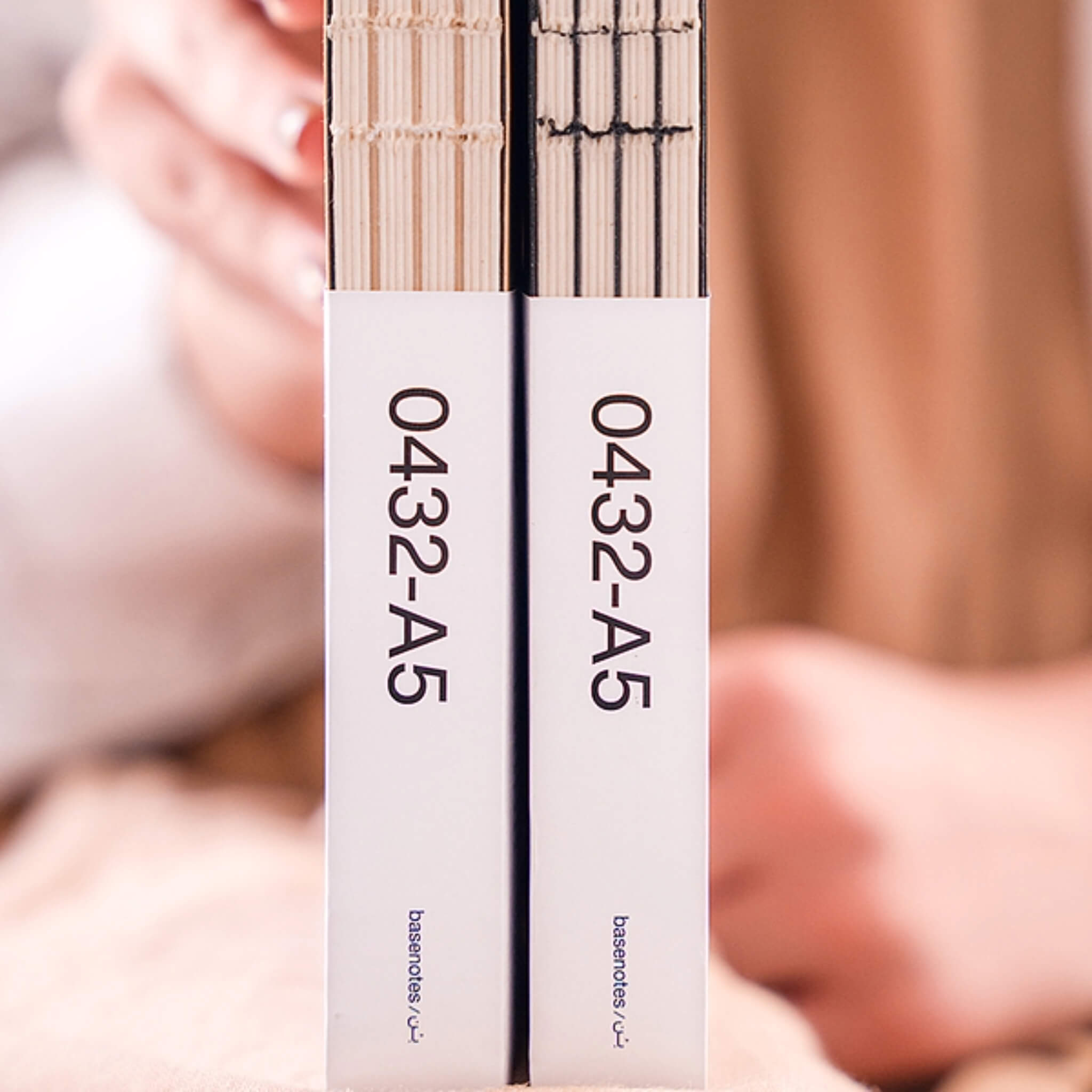 Close-up of two basenotes 0432 A5 Notebooks in kraft and black editions, showing packaging labels and exposed hand-stitched spines.