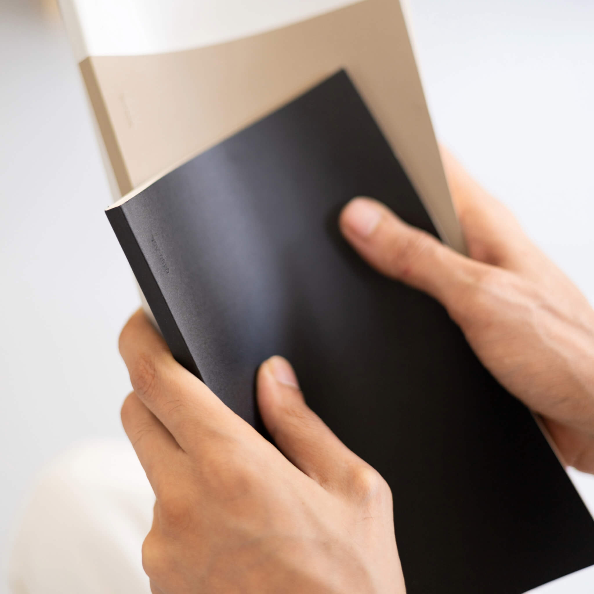 Hands holding basenotes 0480 Notebooks in black and taupe covers, showing slim profile and tactile surface.