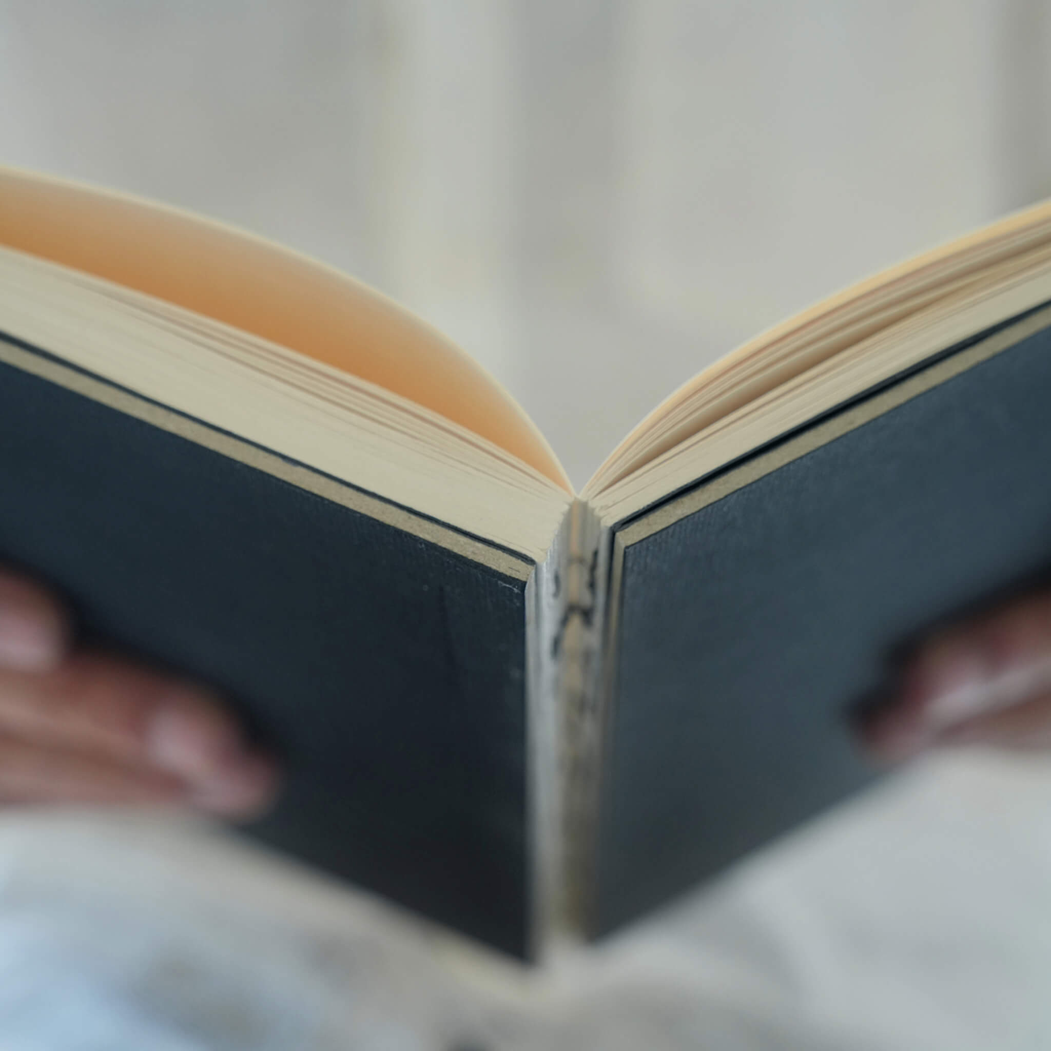 Hands holding an open basenotes 0880 A5 Notebook with a black cover, showcasing lay-flat exposed binding and cream pages.