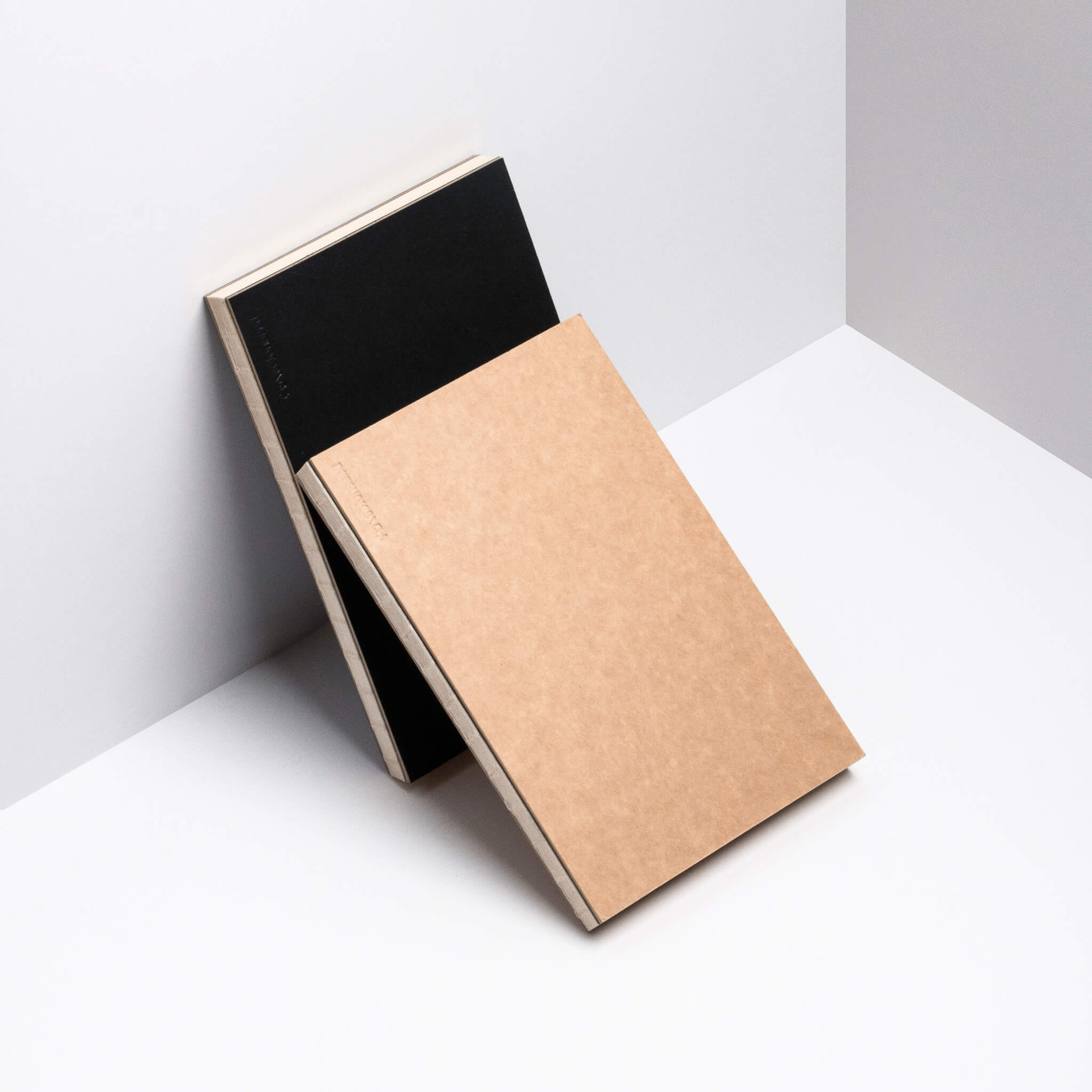 Kraft and black basenotes 0880 Notebooks leaning against a white wall, showcasing exposed thread binding and minimal design.
