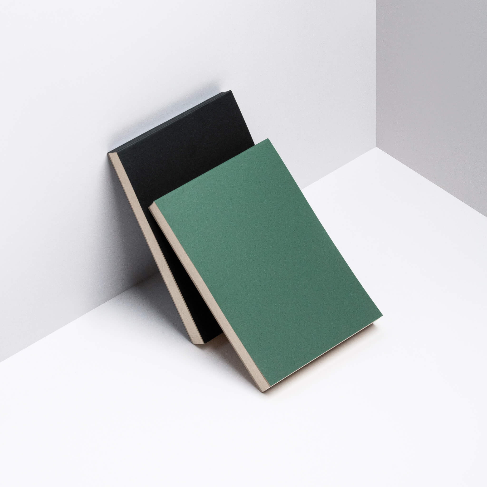 Green and black basenotes 0960 Notebooks leaning together in a minimalist studio setting.