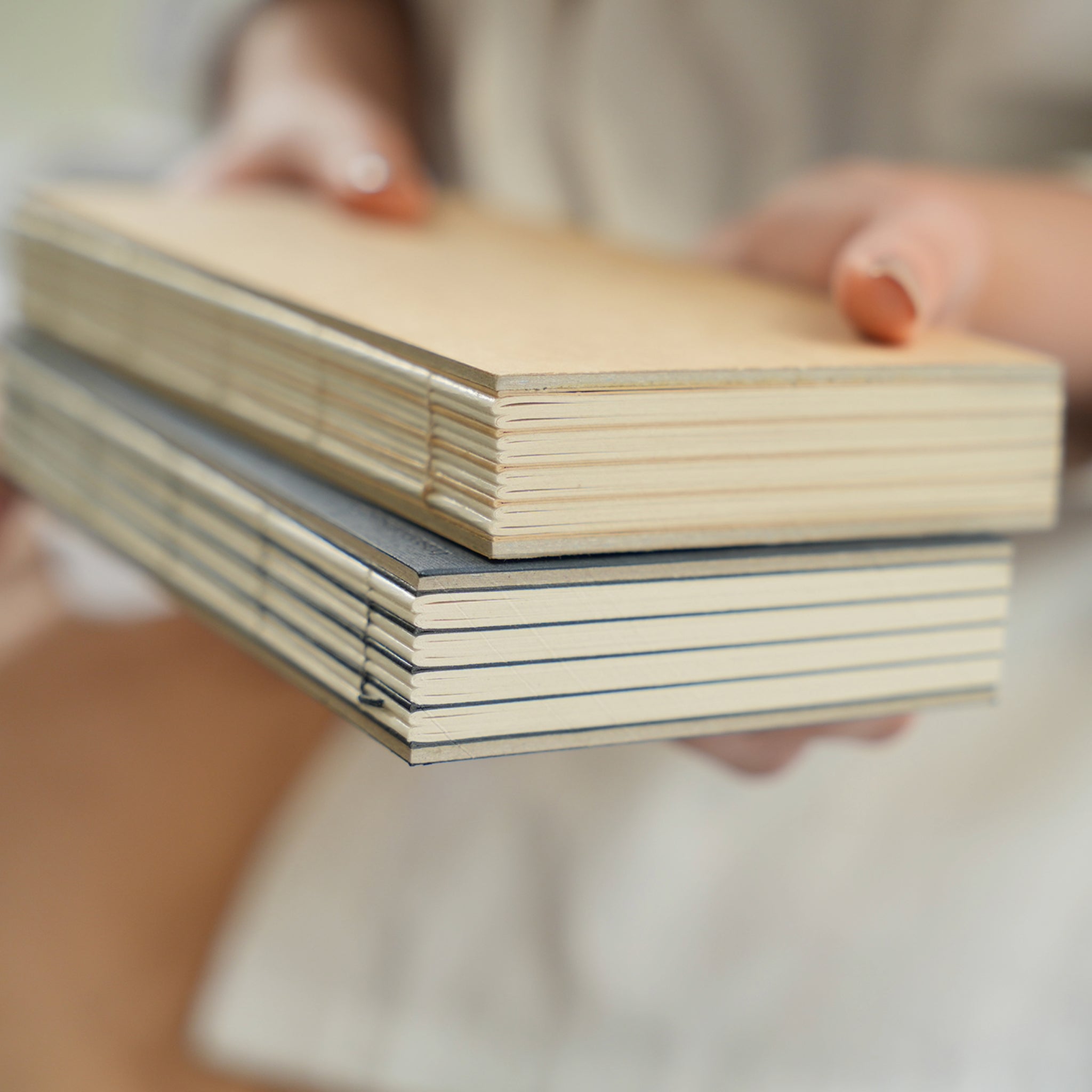 basenotes 1122 Paperbook in Kraft and Pressed Charcoal covers stacked and held by hand, showing exposed binding