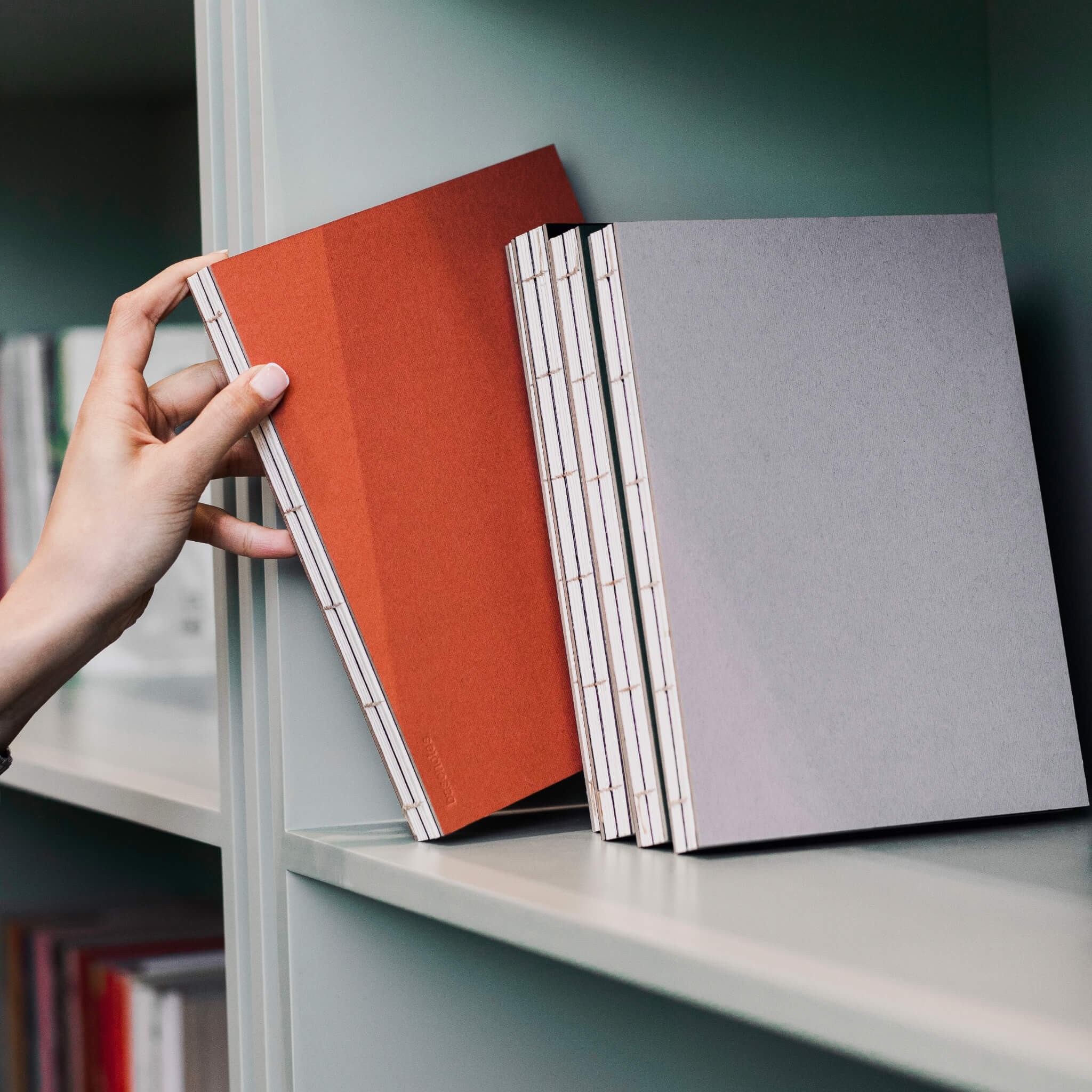 basenotes 1623 Paperbook in clay rust and beige displayed on a shelf, showing exposed hand-stitched spine and minimalist design.