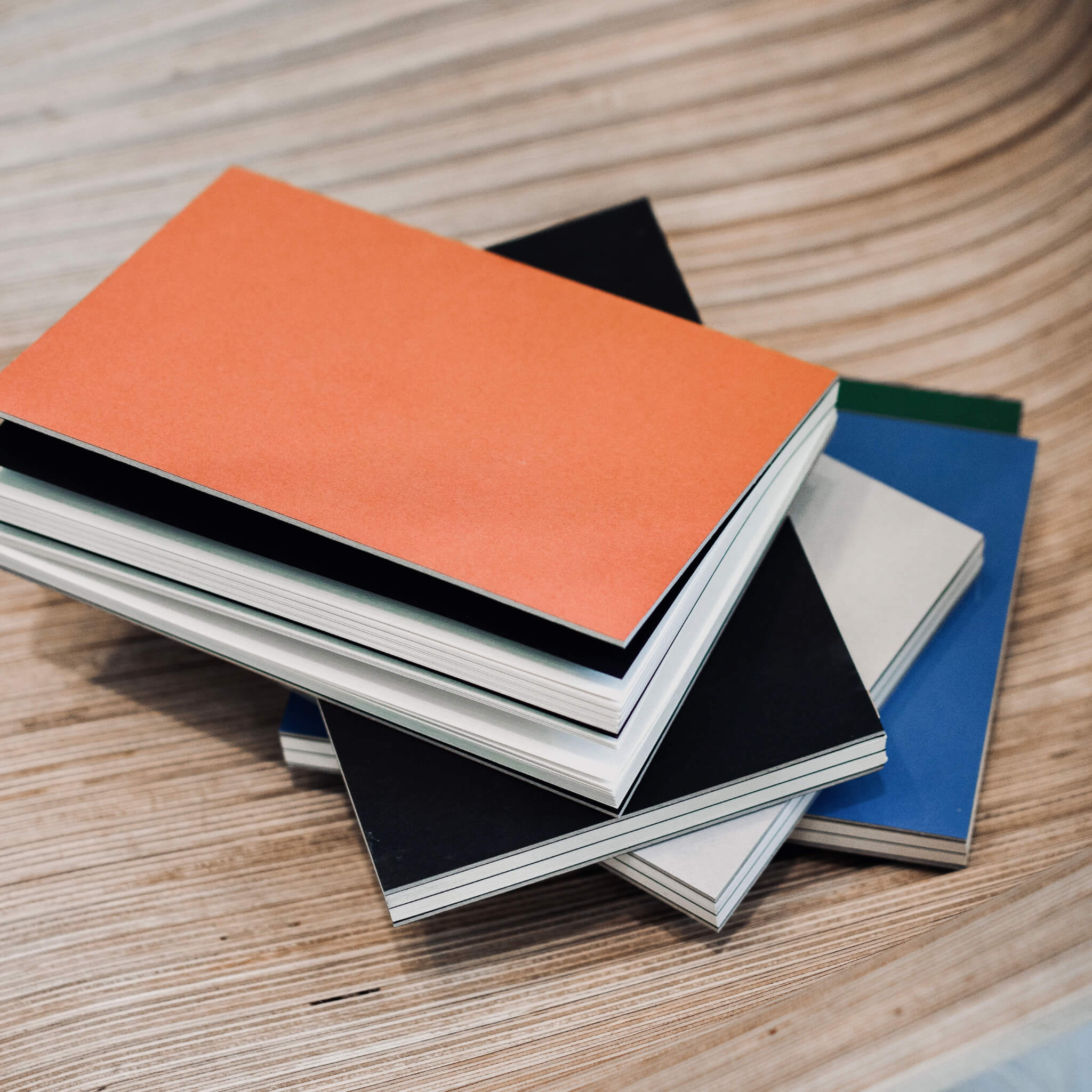 Stack of basenotes 1623 Paperbooks in clay rust, green, blue, beige, and black covers on a wooden table.