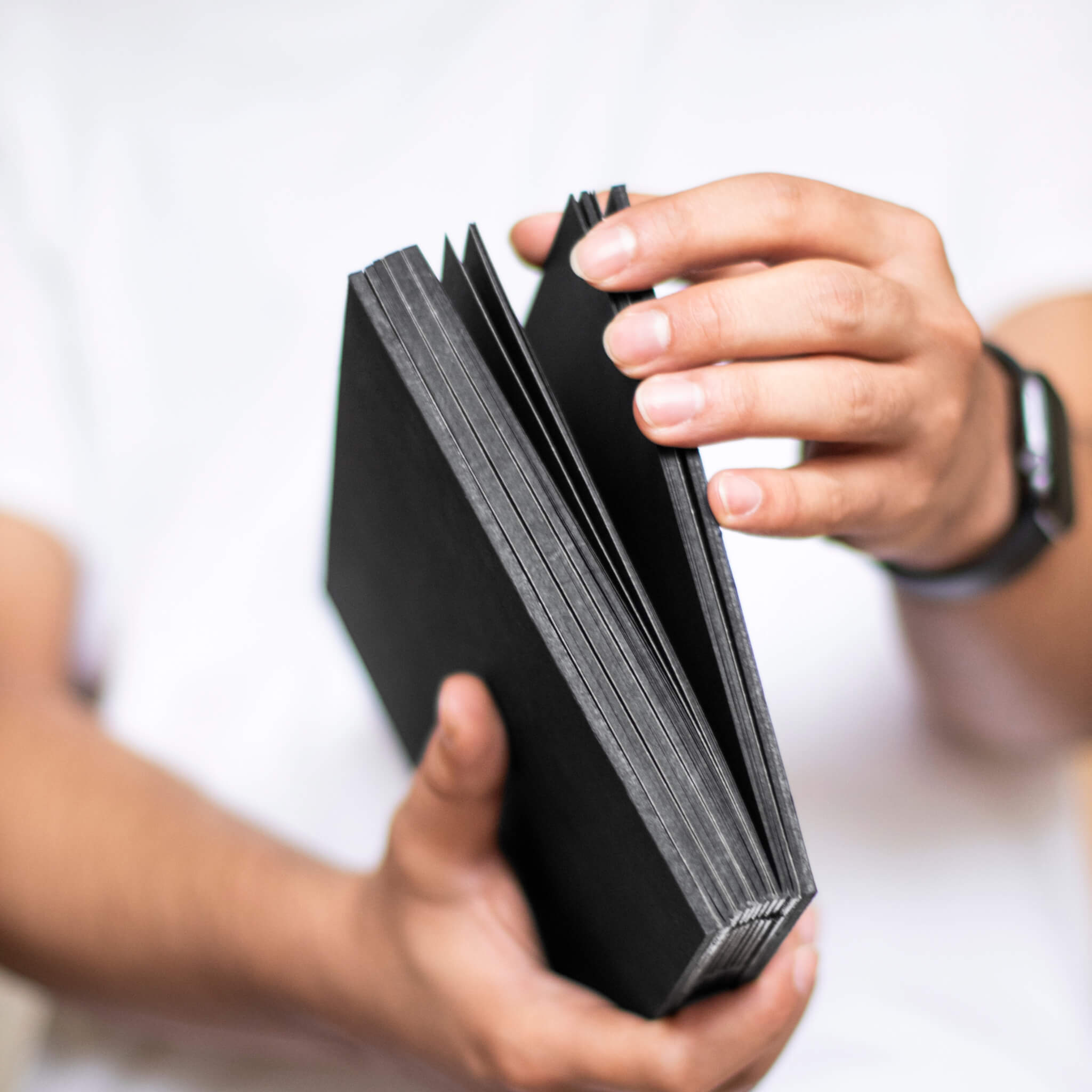 Person holding the basenotes 1623B Black Paper book, showing hand-stitched spine and solid black pages.