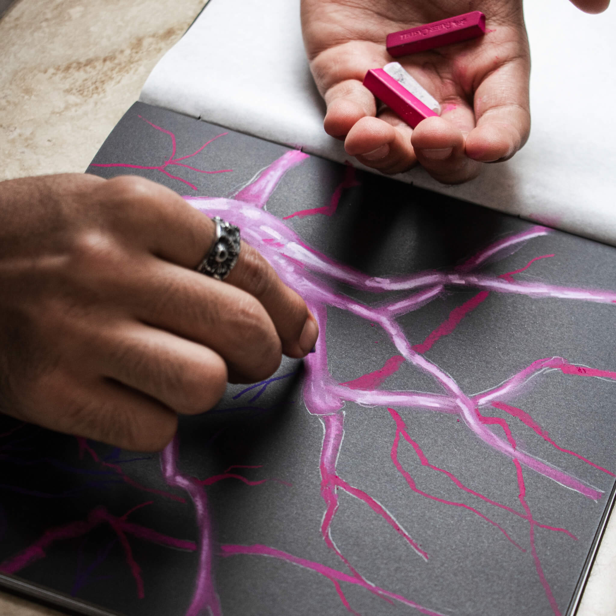 Artist sketching on the basenotes 2222 Black Edition Paper book using pink pastel chalks on textured black paper.