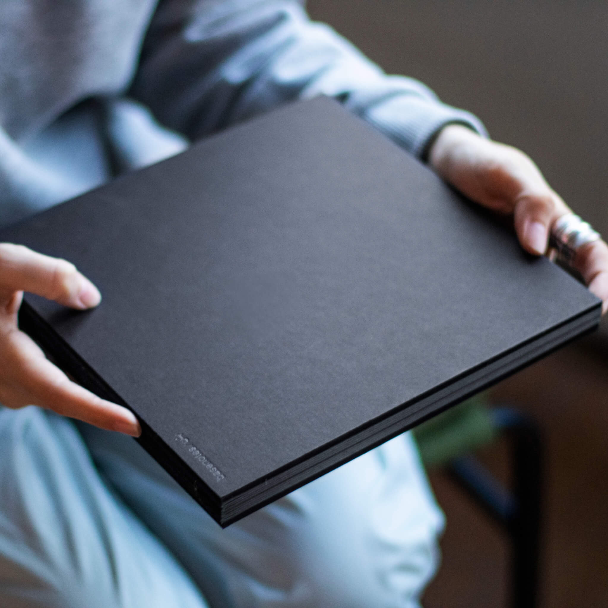 Person holding a closed basenotes 2222 black Paperbook, showing the smooth matte cover and hand-sewn spine.