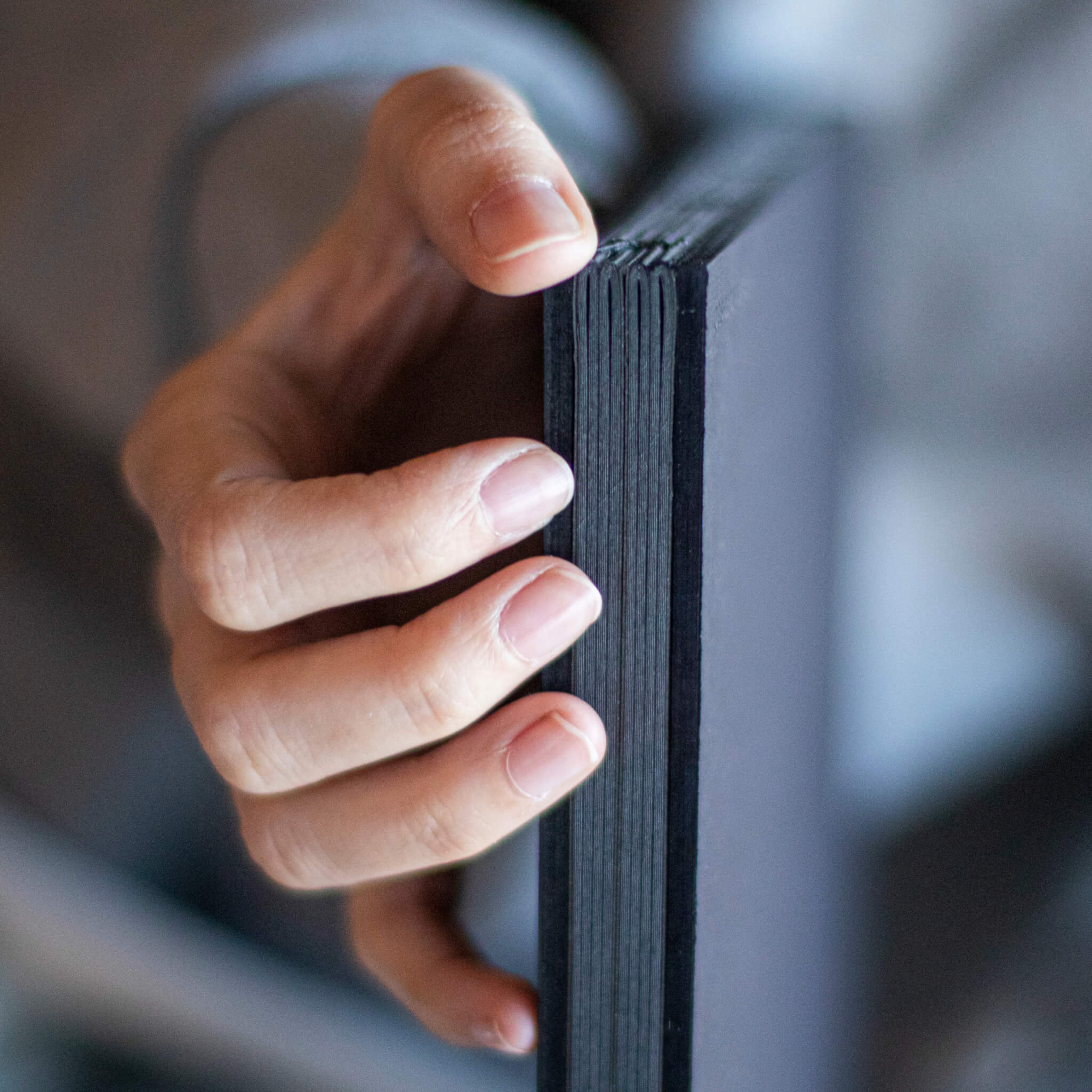 Close-up of a person’s hand holding the basenotes 2222 Paperbook by the spine, showing exposed stitching.