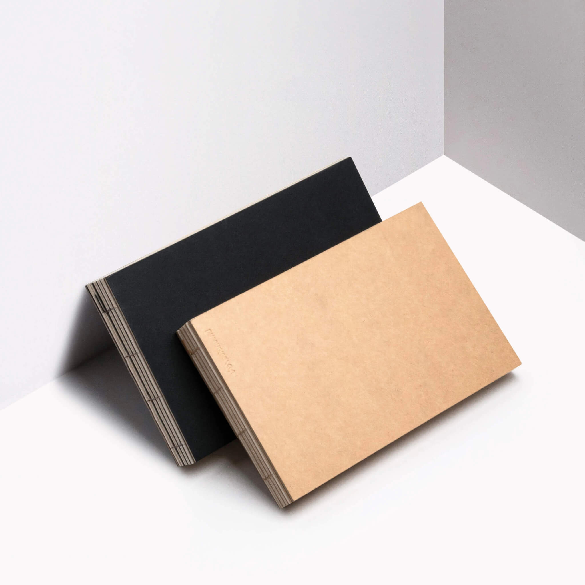 basenotes 2316 sketchbooks in kraft and black covers leaning together, showing exposed stitching.