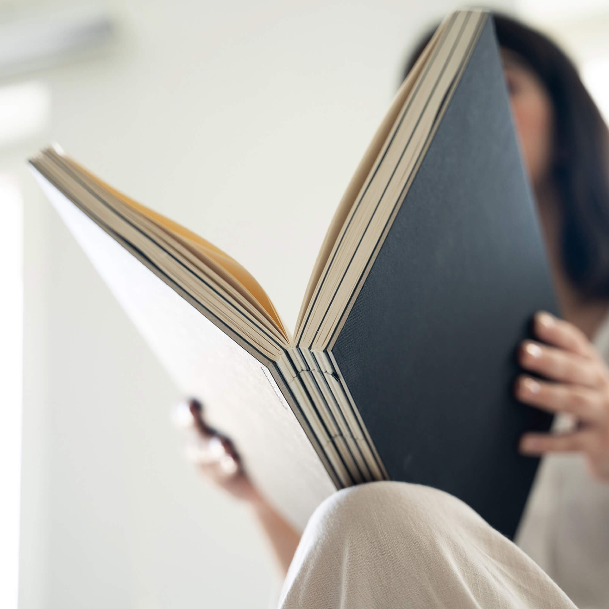 Person holding a basenotes 2333 Paperbook with a black cover, showing exposed spine and layered stitching.