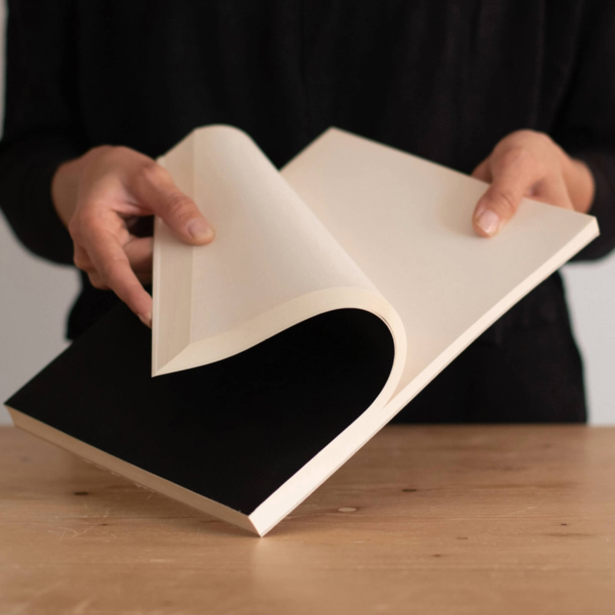 Person holding an open black basenotes 2721 notebook, revealing the smooth FSC-certified cream pages.