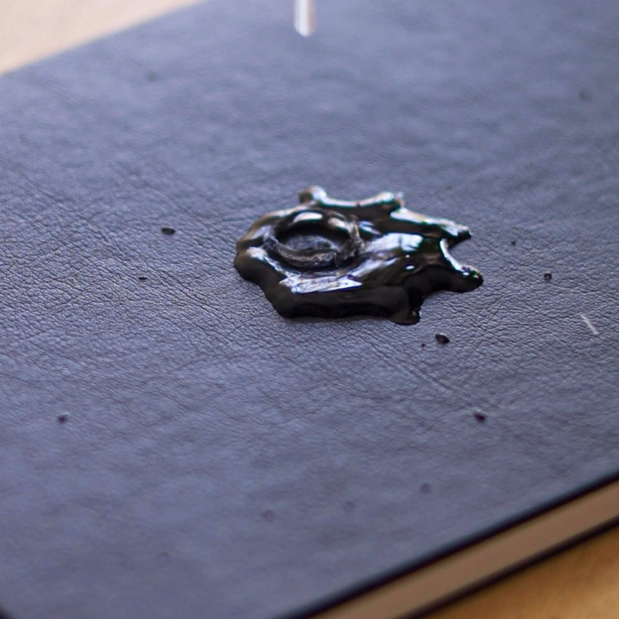Close-up of the basenotes 4000 A5 Notebook’s waterproof black cover with water droplets demonstrating resistance to liquid.