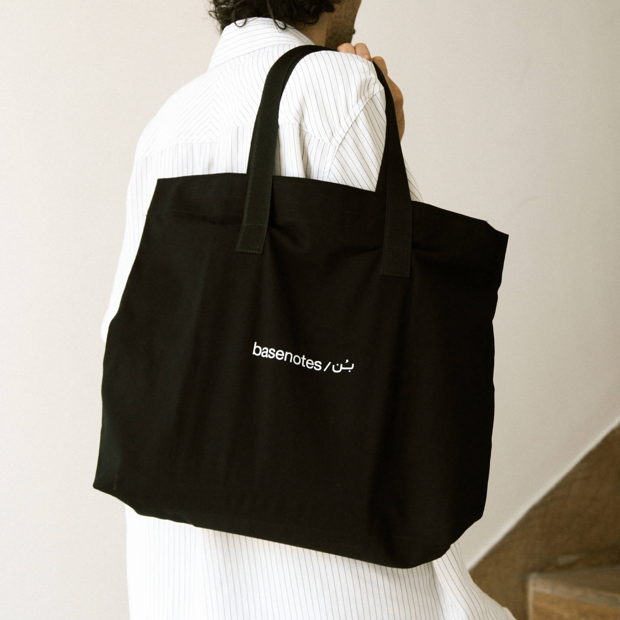 basenotes black fabric tote bag worn over the shoulder, rear lifestyle view