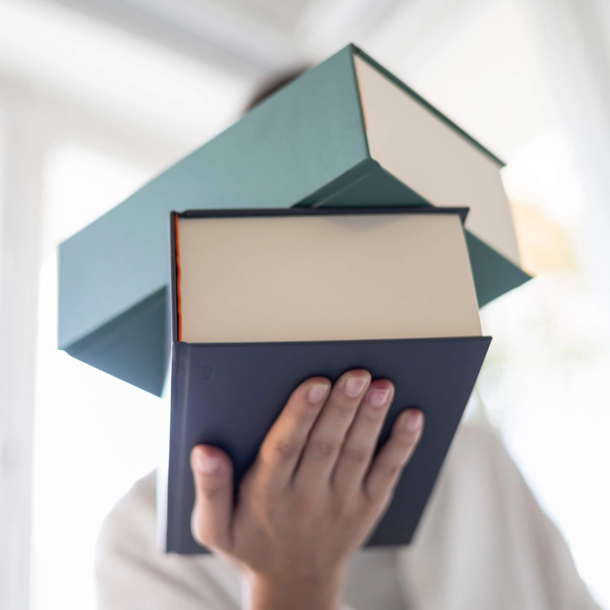 Person holding a stack of basenotes 0512 Notebooks in black and green, emphasising the large-format 1024-page design and solid hardcover.
