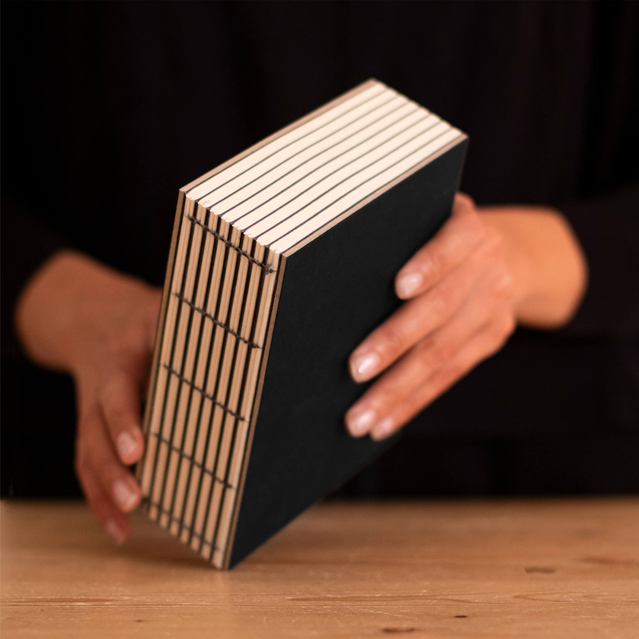 Person holding the Basenotes 1216 Black Paperbook, showcasing the durable hand-stitched binding and minimalist cover.