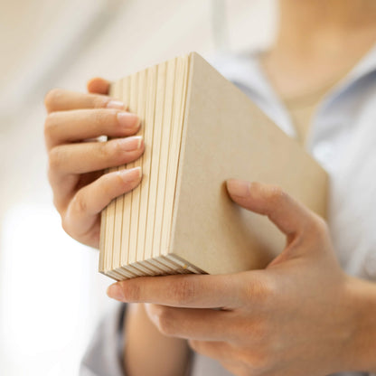 Person holding the basenotes 1216 Paperbook in Kraft cover, showing the hand-stitched spine and natural texture.