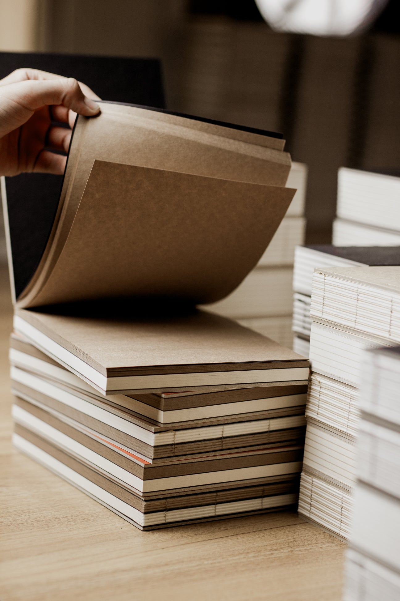 Stack of basenotes sketchbook brown books with a hand flipping through one, on a wooden surface. basenotes.co