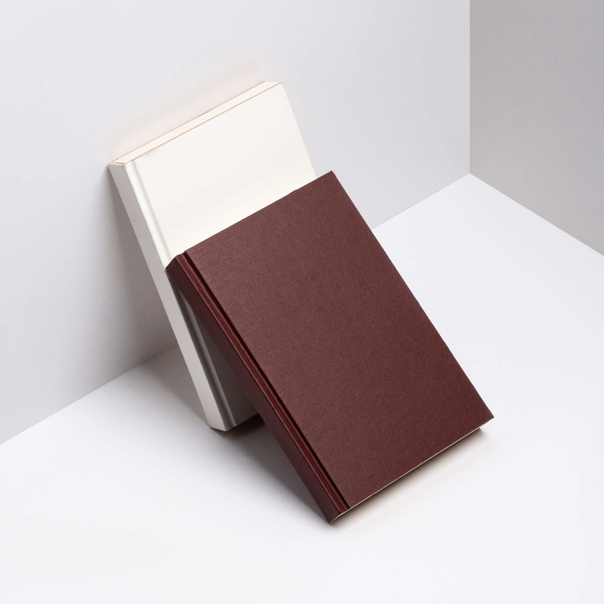 Maroon and white basenotes 0128 Notebooks leaning together against a neutral background.