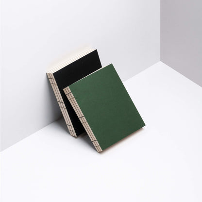 basenotes 0144 notebooks in green and black covers leaning together, featuring exposed spine stitching and minimal aesthetic.