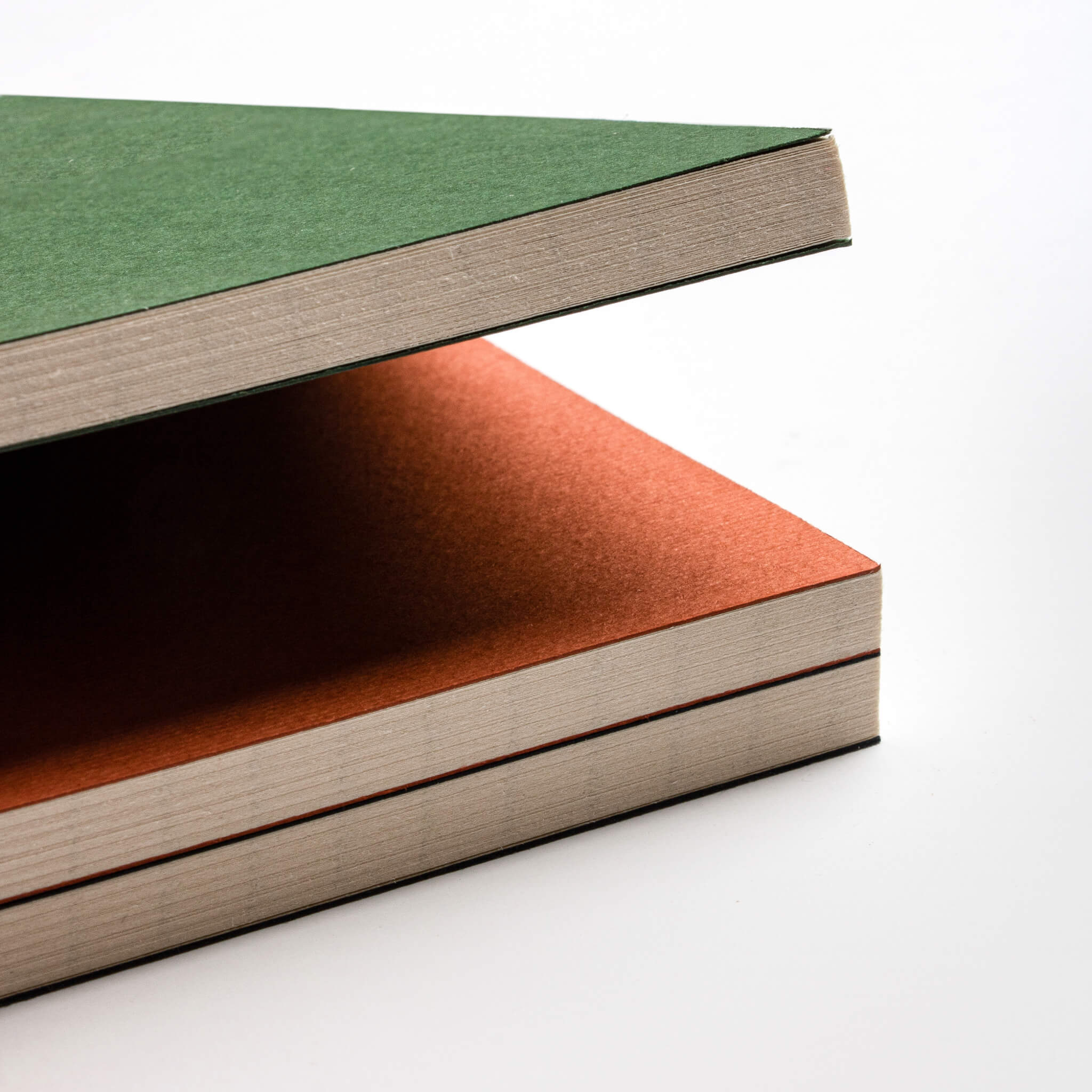 basenotes 0144 Notebooks stacked in green and orange covers, highlighting smooth matte finish and hand-stitched edges.