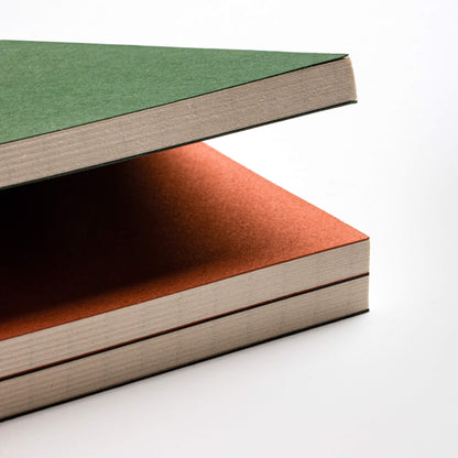 basenotes 0144 Notebooks stacked in green and orange covers, highlighting smooth matte finish and hand-stitched edges.