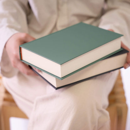 Person holding two basenotes 0256 A5 Notebooks in green and black covers, showing their sturdy hardcover and clean design