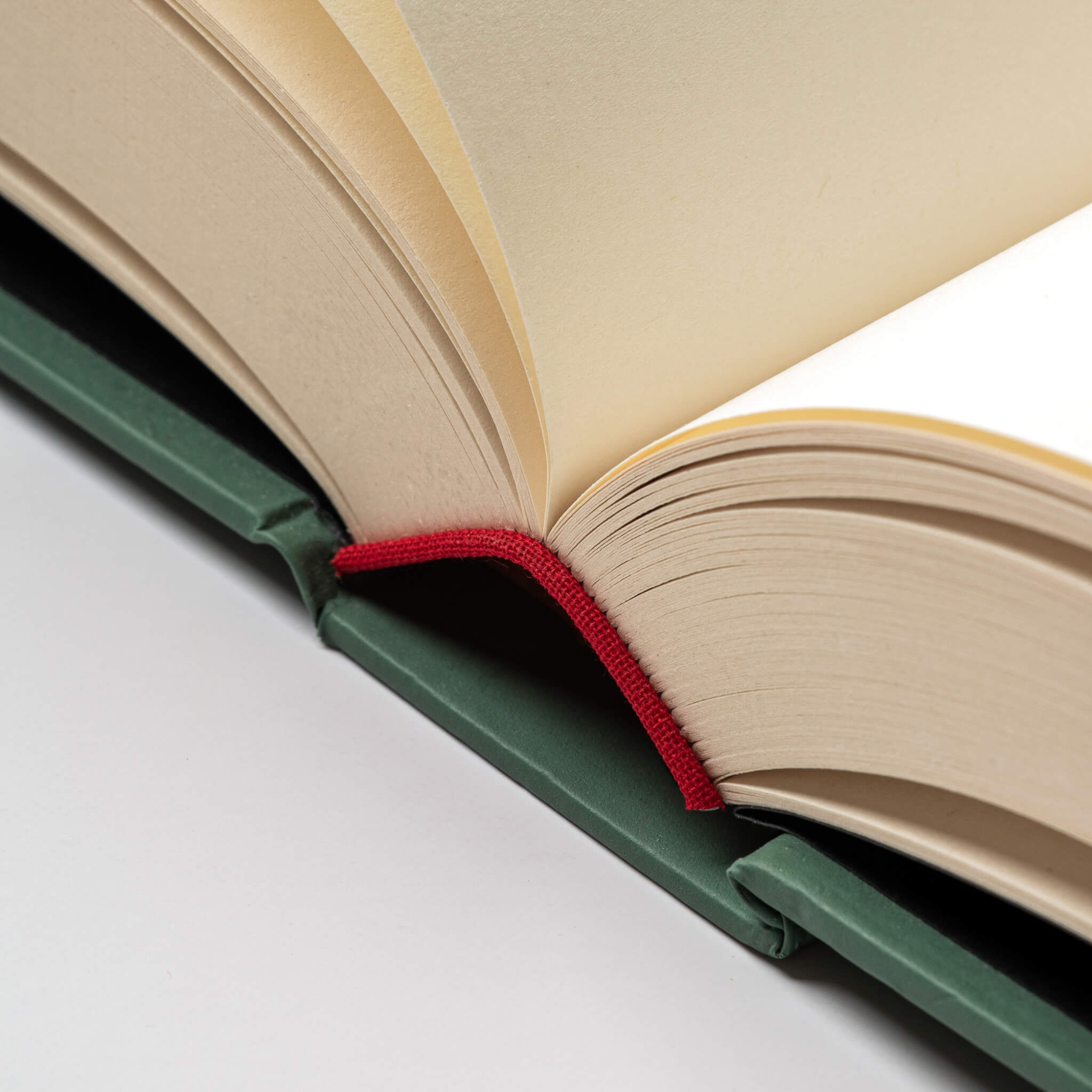 Macro shot of the basenotes 0256 Notebook’s red cloth spine and green hardcover, showing precise binding and smooth paper texture.