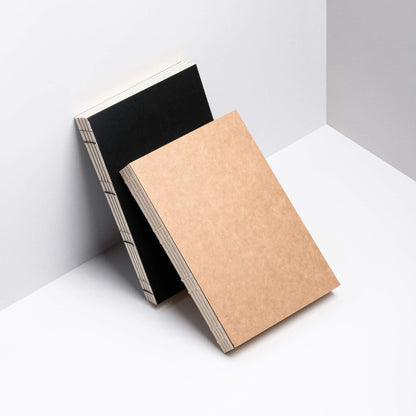 Black and kraft Basenotes 0432 Notebooks leaning against a wall, showcasing exposed thread binding.
