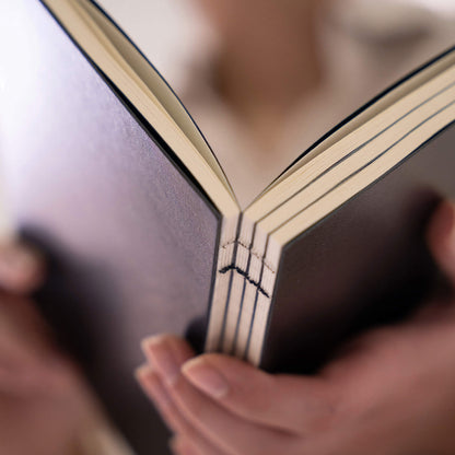 Person holding an open basenotes 0432 Notebook with a black cover and visible hand-sewn spine.