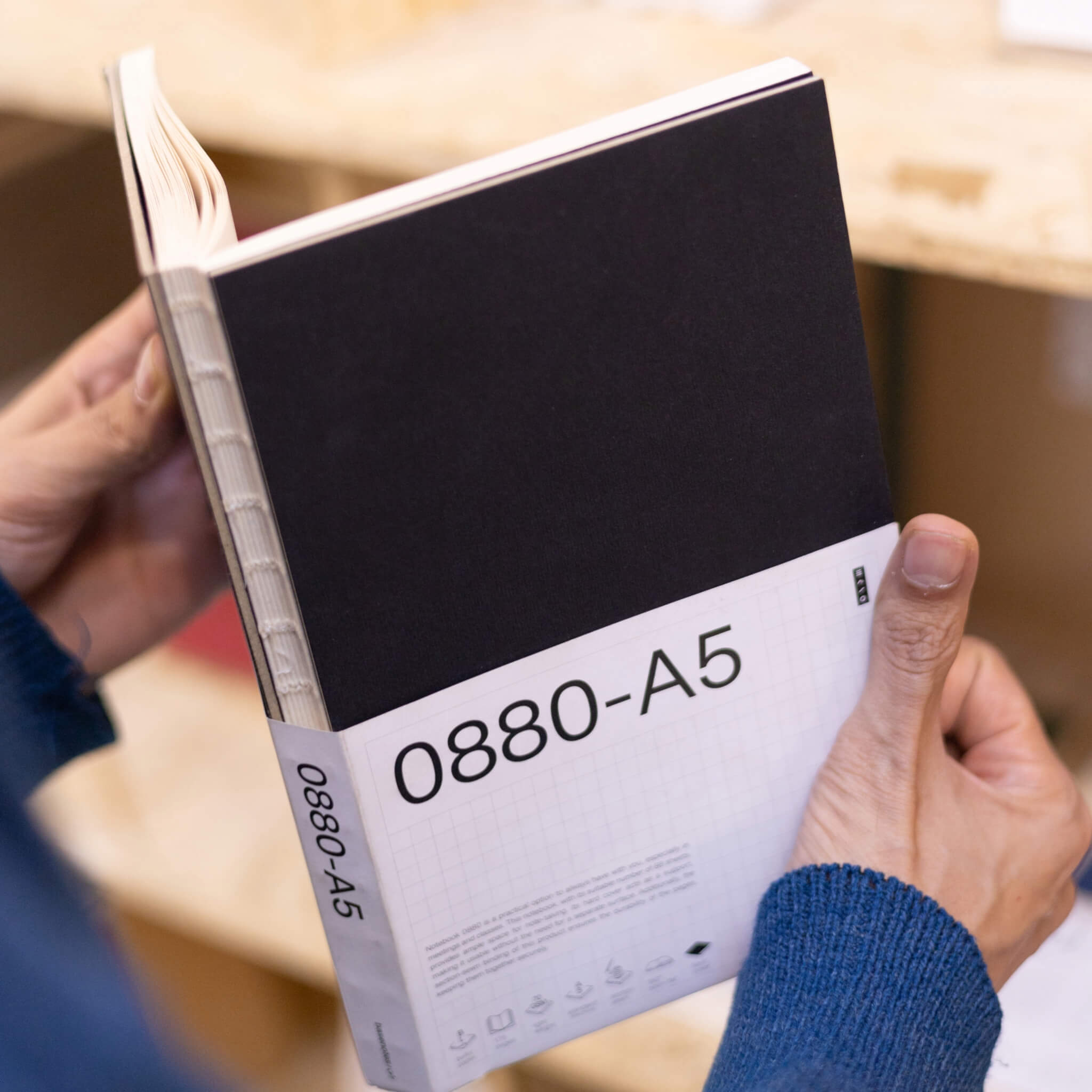 Person holding a basenotes 0880 A5 Notebook with a black cover and white sleeve, displaying exposed spine and craftsmanship