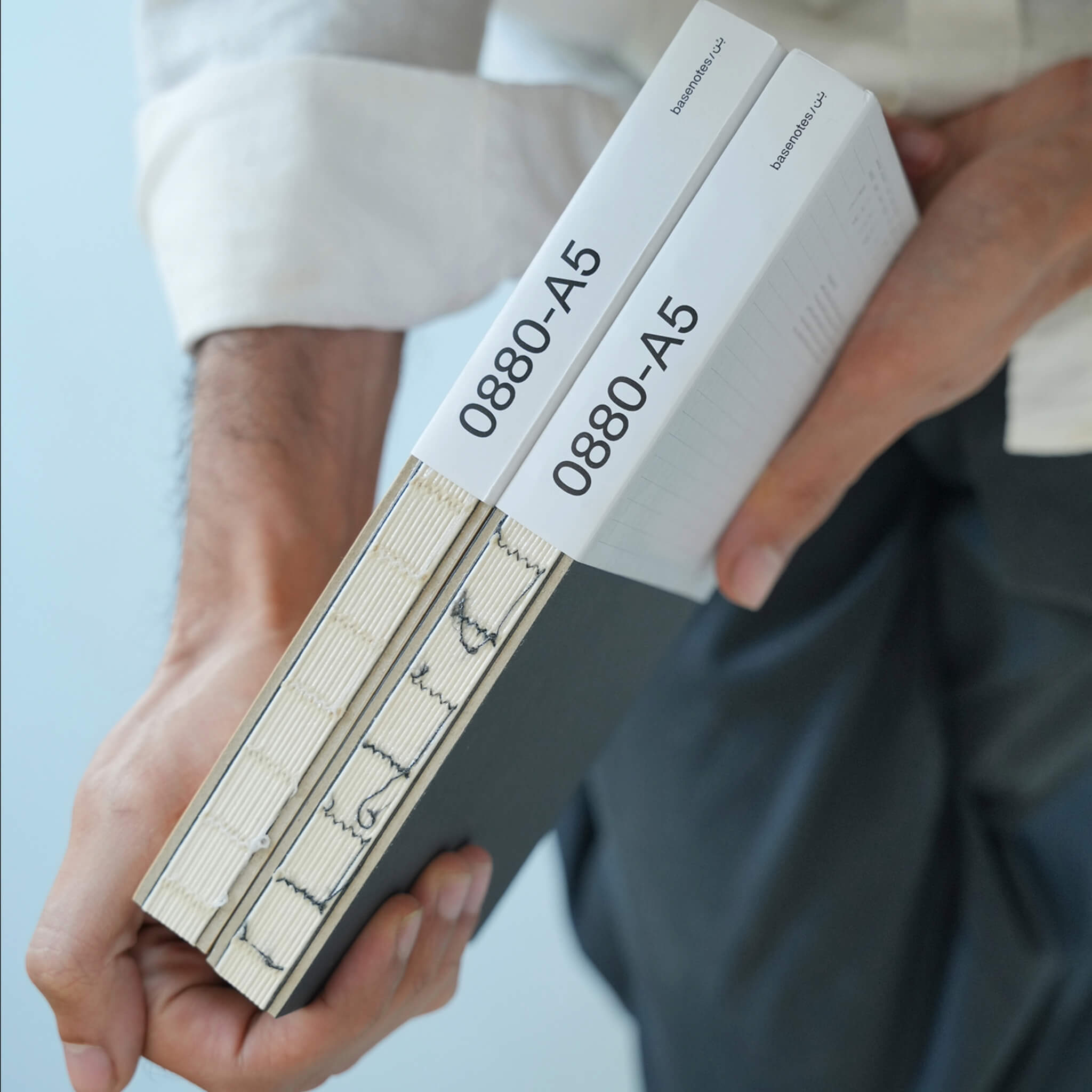 Close-up of two basenotes 0880 A5 Notebooks with white sleeves showing the product code and visible stitching detail.