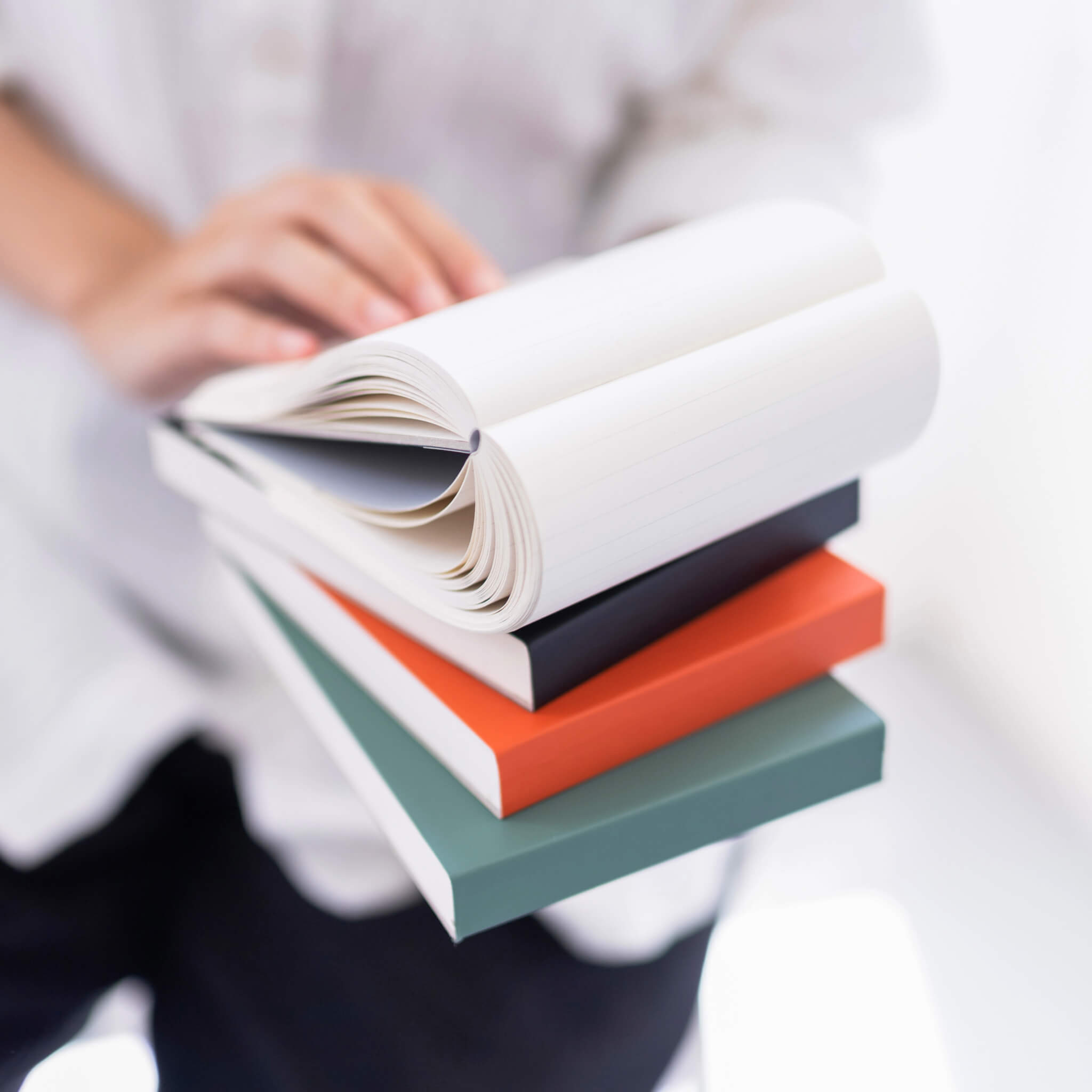 Open basenotes 0960 Notebook resting on a stack of colourful covers, showing lay-flat design and lined pages.