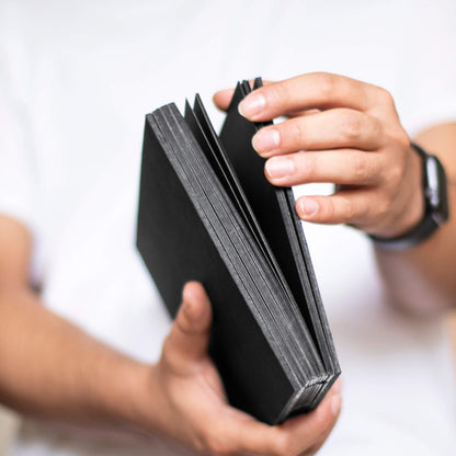 Person holding the basenotes 1623B Black Paper book, showing hand-stitched spine and solid black pages.