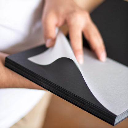 Person holding basenotes 1623B Black Paper book and turning tracing paper between black pages.