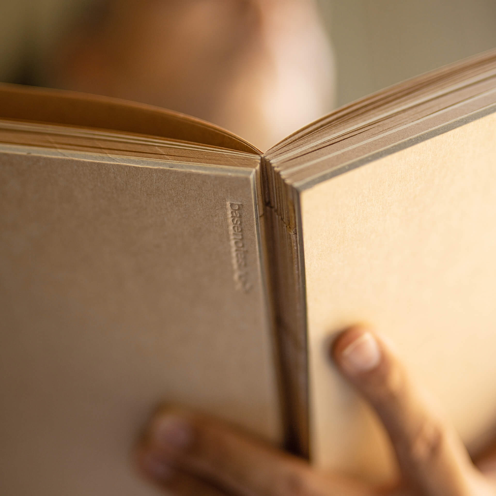 Close-up of basenotes 1623K Kraft Paper book cover held in hand, showing embossed logo detail.