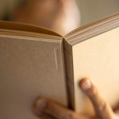 Close-up of basenotes 1623K Kraft Paper book cover held in hand, showing embossed logo detail.
