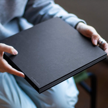 Person holding a closed basenotes 2222 black Paperbook, showing the smooth matte cover and hand-sewn spine.