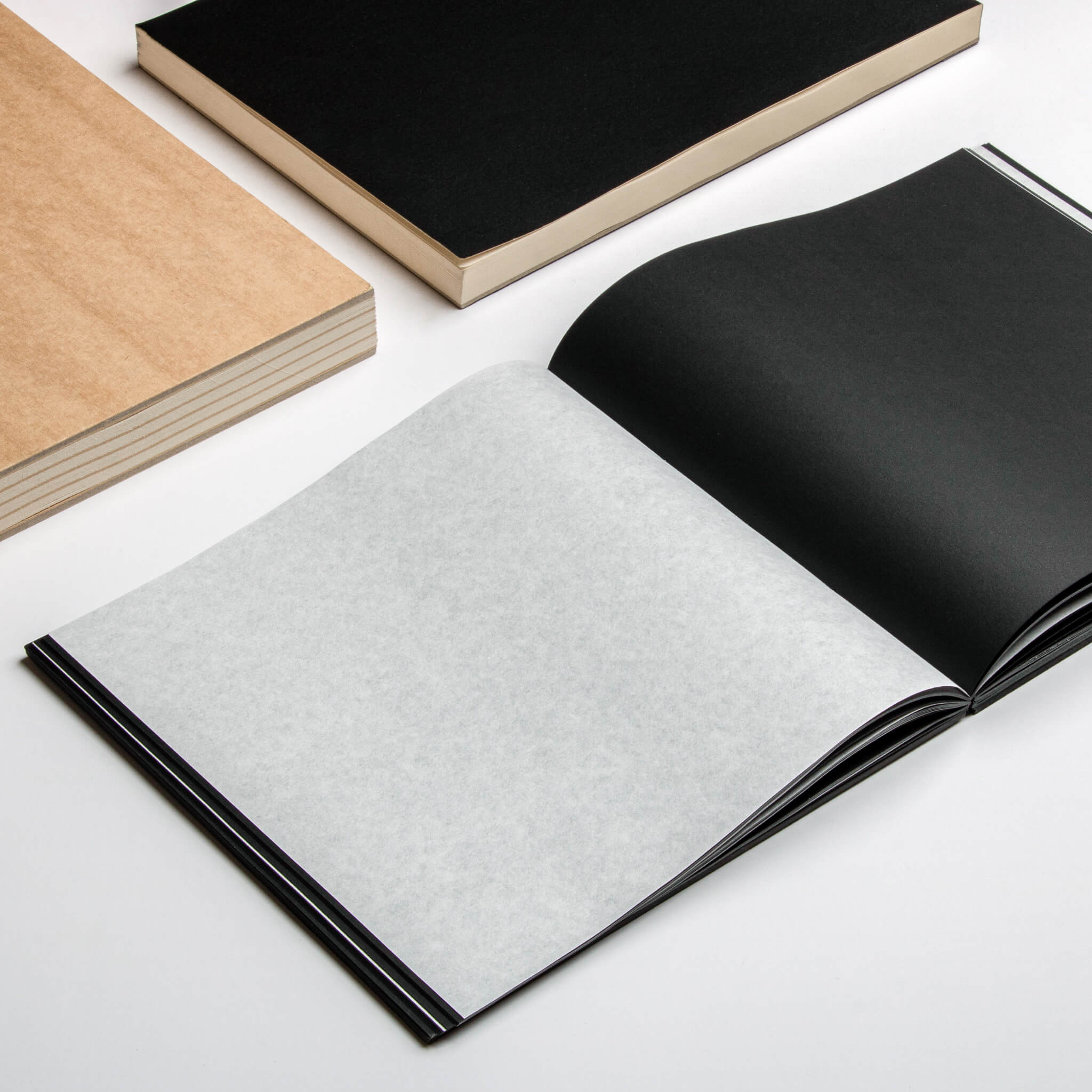 Open basenotes 2222 Paperbook showing black pages interleaved with tracing paper and a kraft notebook beside it.