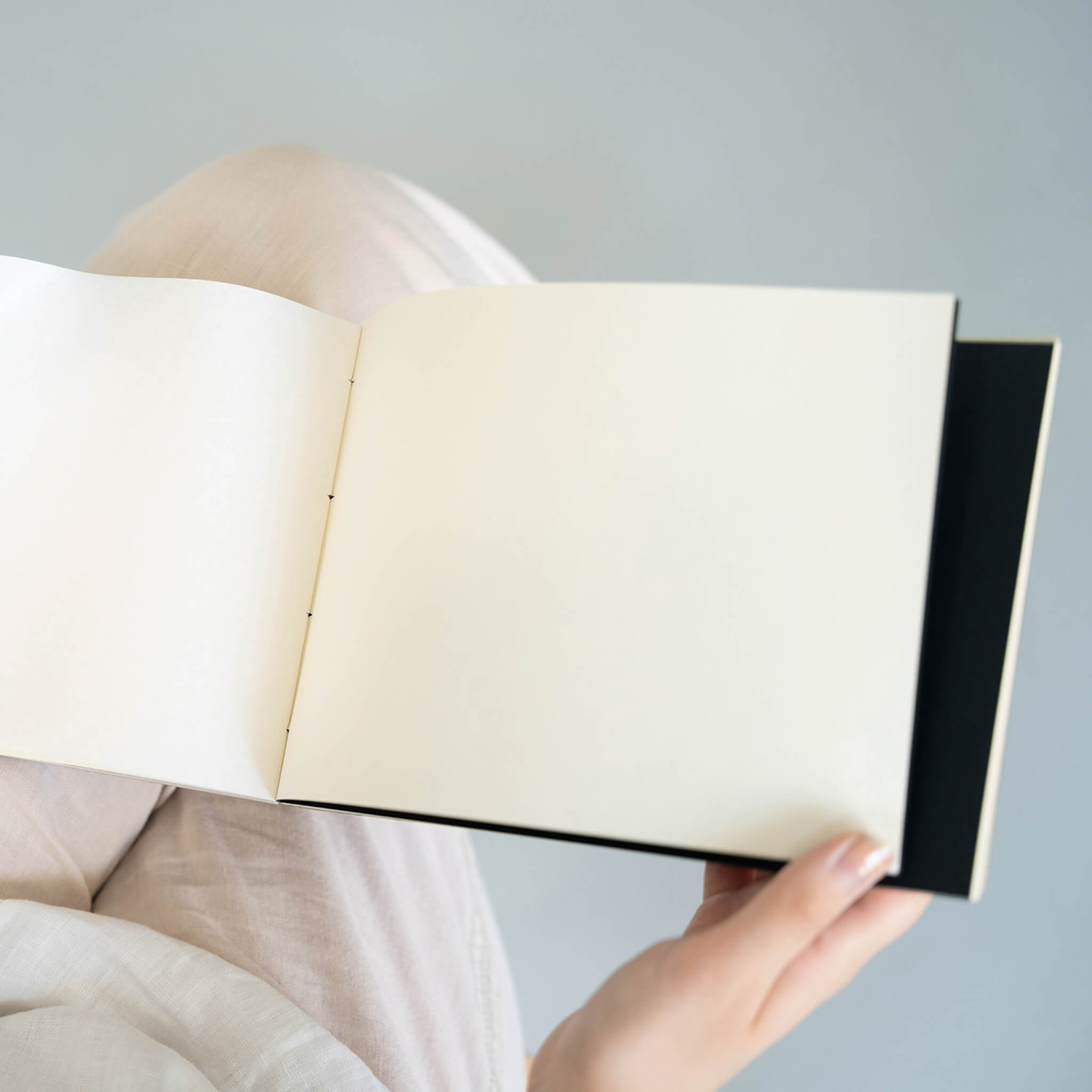 Open basenotes 2316 sketchbook resting on a lap, showing smooth cream pages and hand-stitched binding.