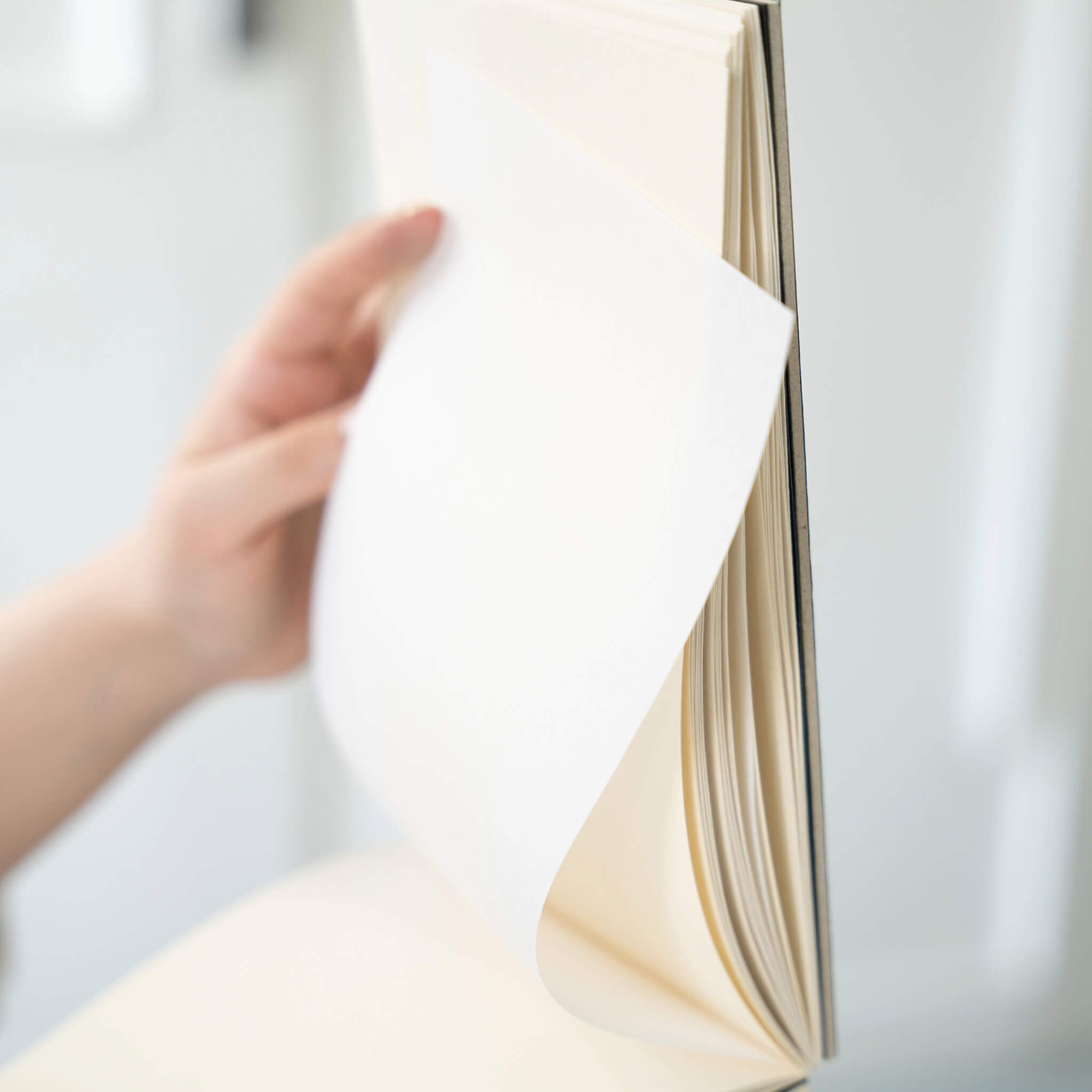 Close-up of a hand turning a page in the basenotes 2316 sketchbook, revealing interleaved tracing paper and textured pages.