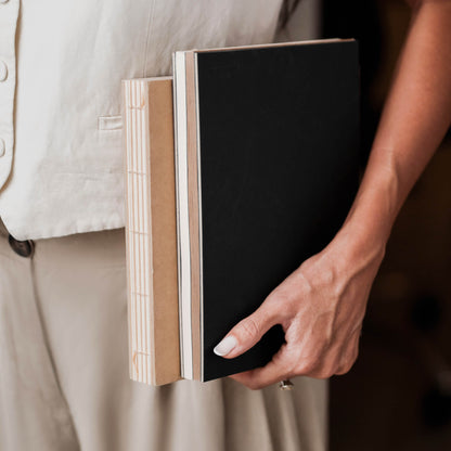 Person holding basenotes 2316M Paper books in black and kraft covers, showing exposed hand-stitched spines.
