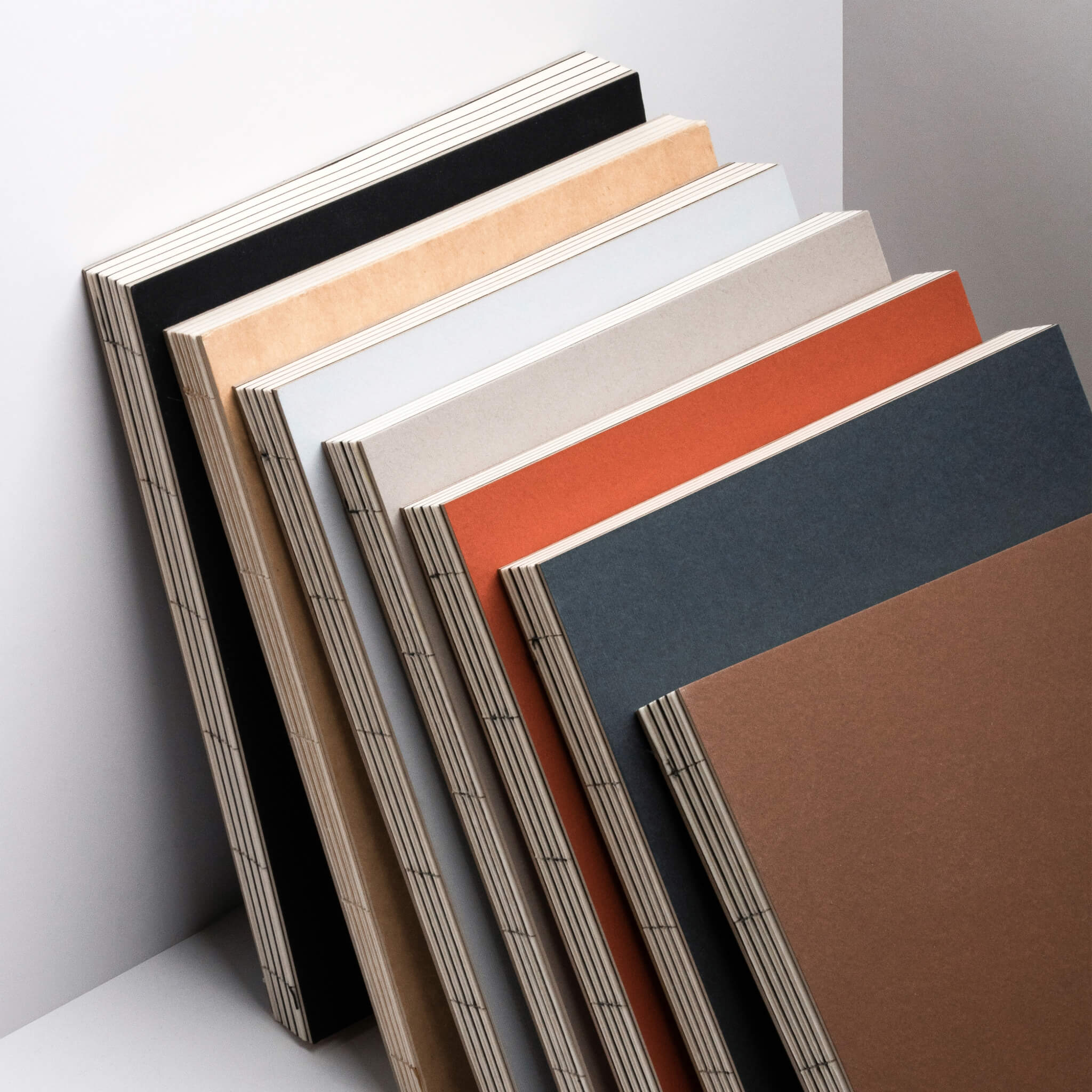 Line-up of basenotes 2333 Paperbooks in multiple colours black, kraft, rust, charcoal, mist, beige, and brown — all with exposed binding.