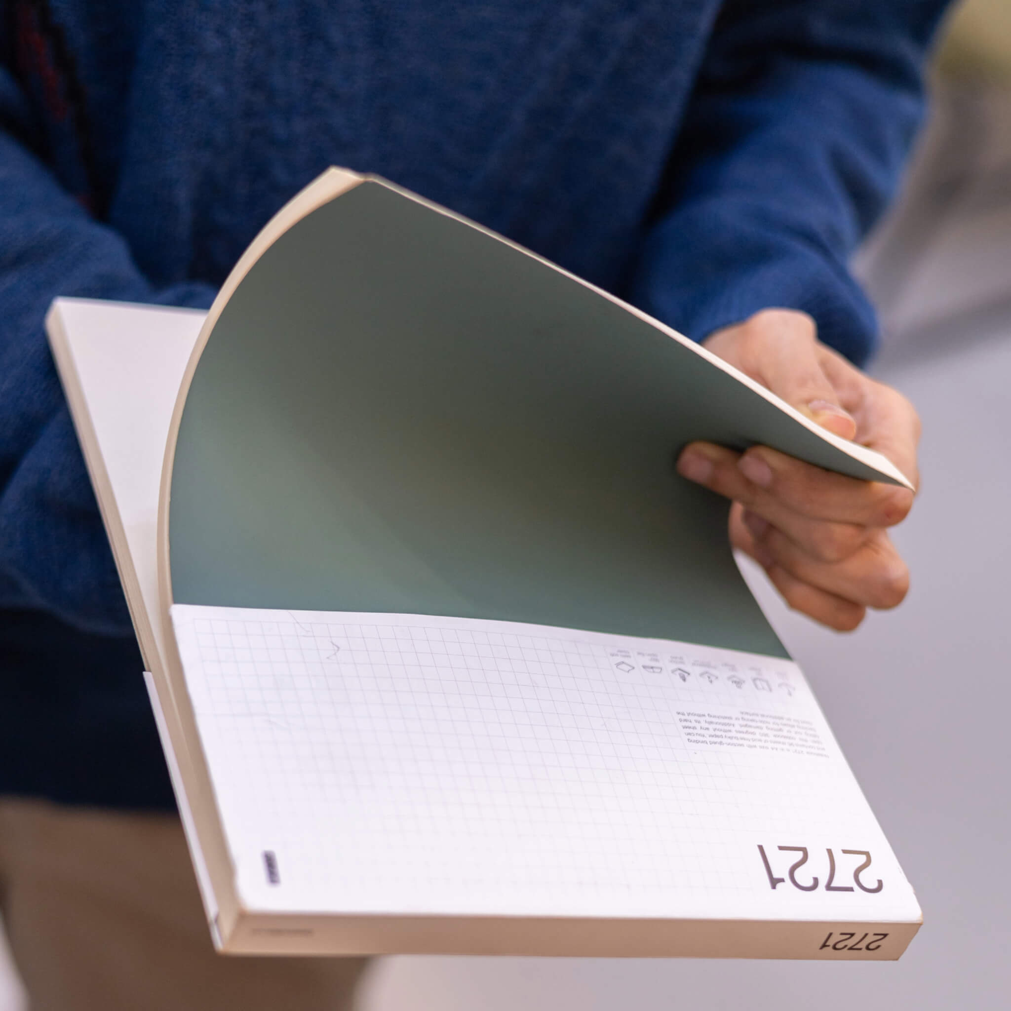 Person holding a green basenotes 2721 notebook with its branded sleeve, showing the minimalist grid design and FSC-certified details.